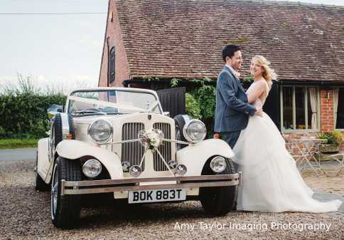 Bride and Groom posing for a photo beside the Beauford wedding car at Curradine barns.