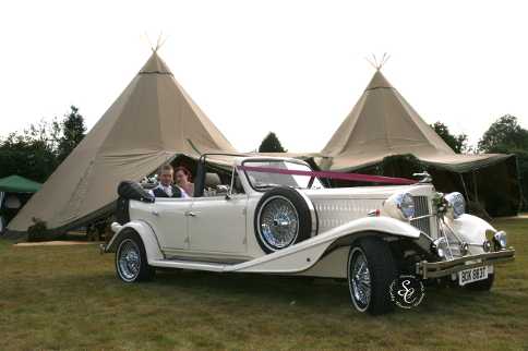 Bride and Groom sat in the Beauford wedding car with two Tepees in the background.